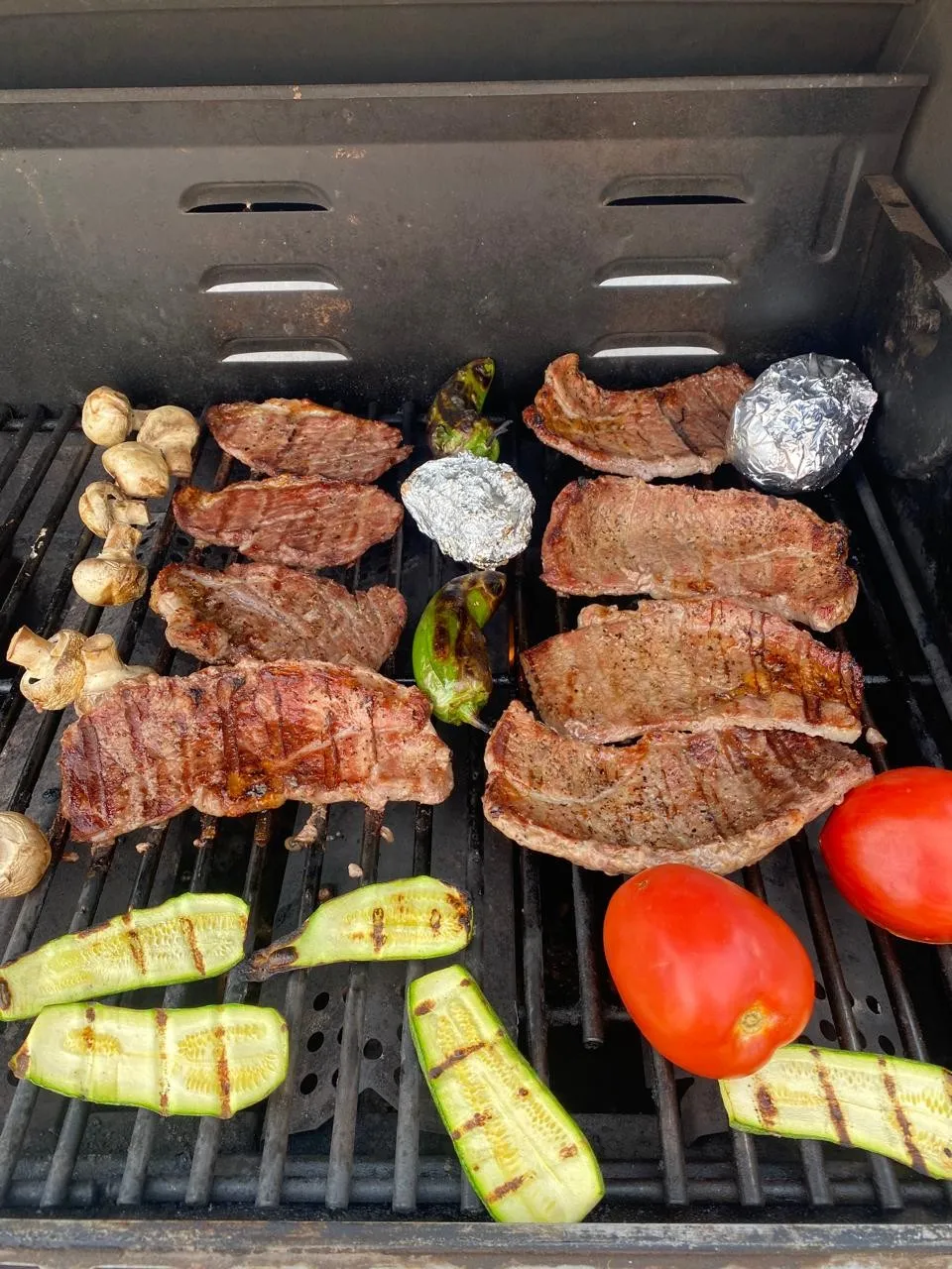 Asador con cortes de carne, champiñones, calabacitas, jitomates, chiles y papas en papel aluminio