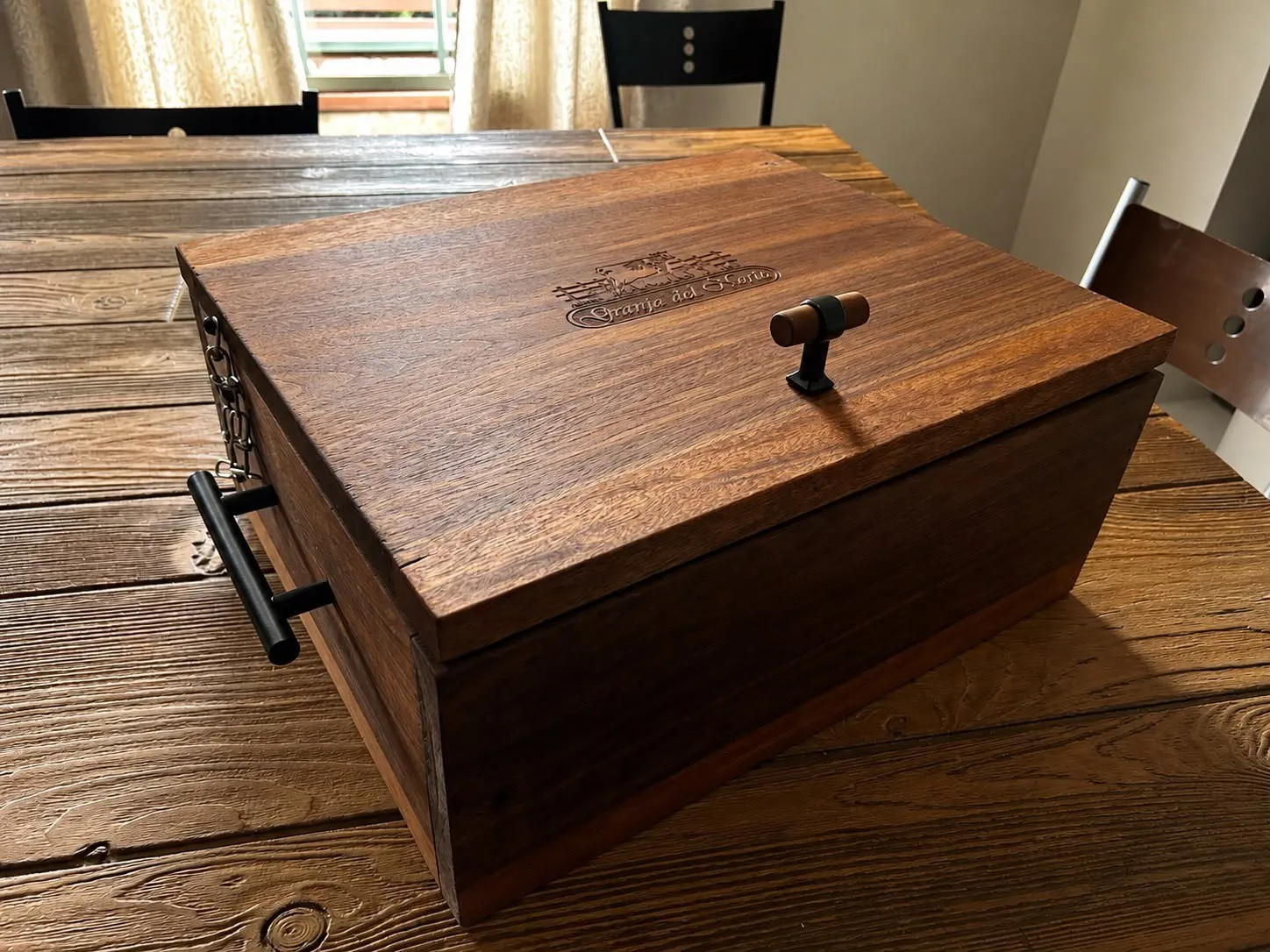 Grill Box de nogal cerrada sobre una mesa de madera, con el grabado de Granja del Norte en la tapa