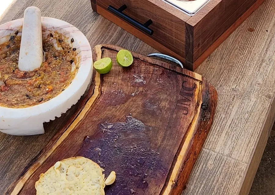 Tabla de madera con limones y pan, junto a un molcajete con salsa